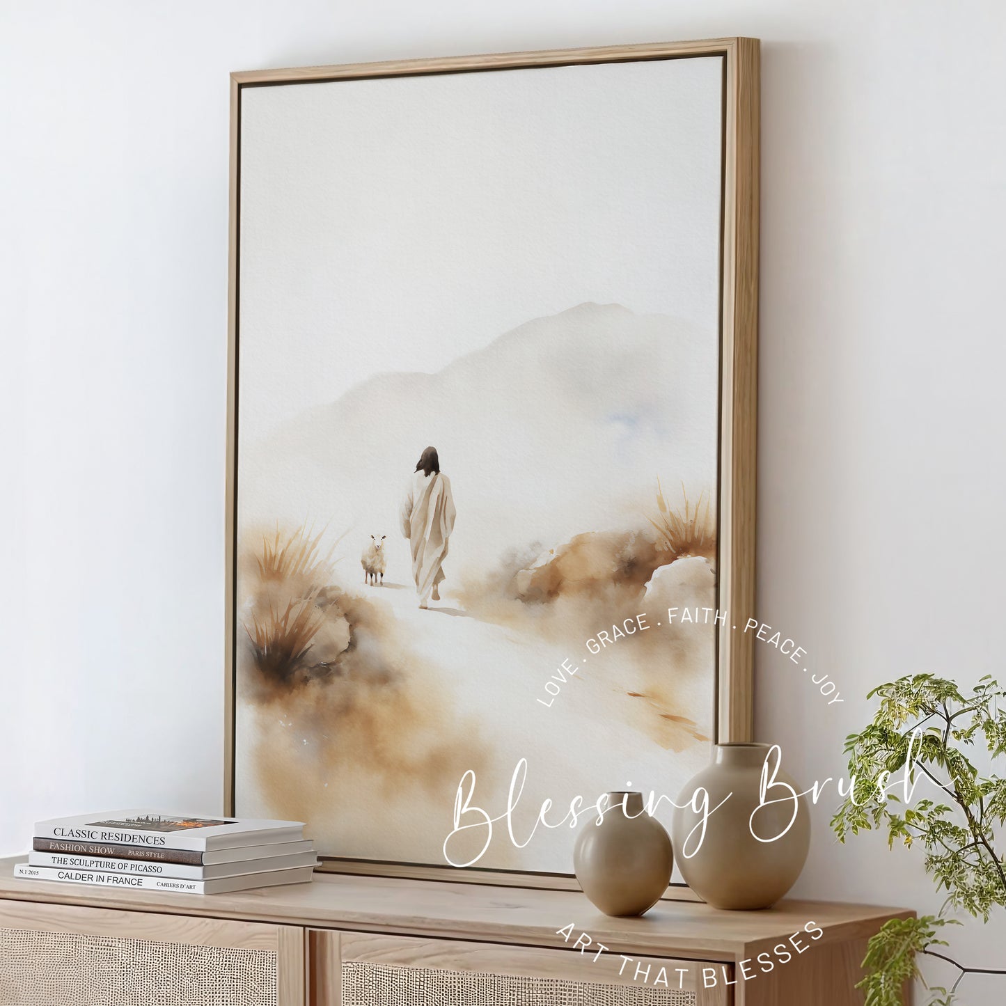 Framed Christian watercolor canvas of Jesus found lost sheep, styled on a neutral console table with modern vases and books, Blessing Brush wall art.